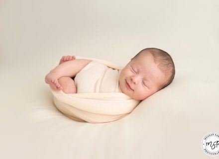 Newborn baby swaddled on peach background. At Meagan Sarah Photography.
