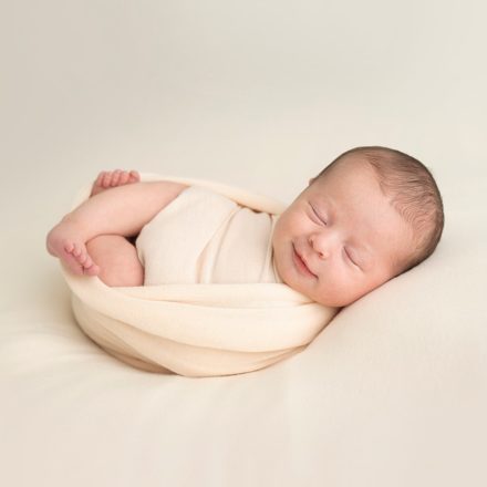 Newborn baby swaddled on peach background. At Meagan Sarah Photography.