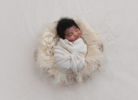 Beautiful newborn baby in swaddle on cream fur