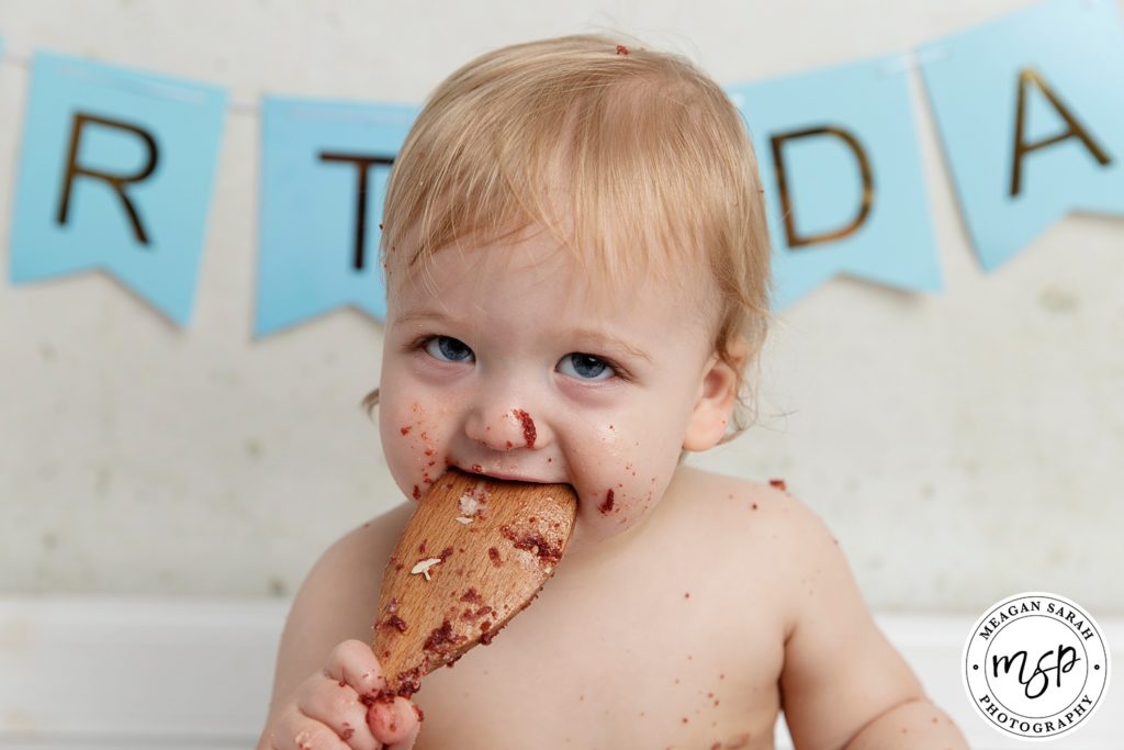 Funny cake smash photo little boy eating a spoon covered in chocolate cake in our studio Leeds