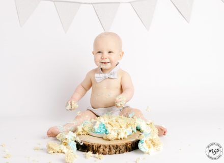 Cake Smash, Baby boy with silver bunting and grey outfit on wooden stand, Leeds,