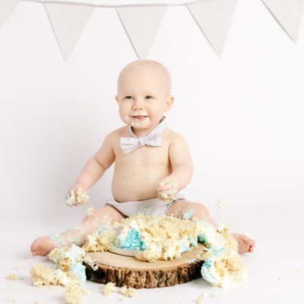 Cake Smash, Baby boy with silver bunting and grey outfit on wooden stand, Leeds,