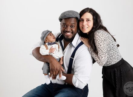 mum, dad and baby facing camera. dad and baby in flat caps and braces mum dressed in leopard print top and black trousers on a white background