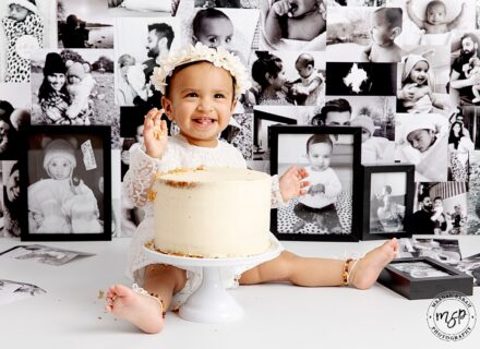 Adorable baby girl with flower crown on at her cake smash. Photo wall as background.