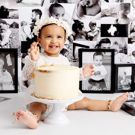 Adorable baby girl with flower crown on at her cake smash. Photo wall as background.