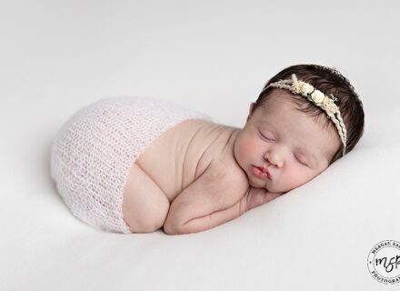 Little baby newborn girl laying on her front with a headband.