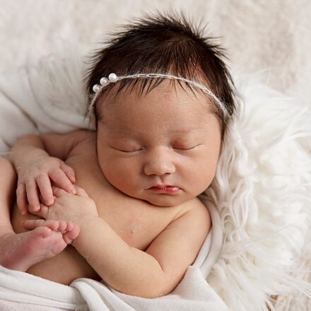 A beautiful, dark hair baby with headband on, laying on fur rug, asleep in a fruit bowl.