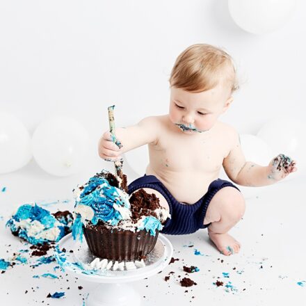 Little boy smashing a blue chocolate cake up with a wooden spoon at his cake smash photo session.