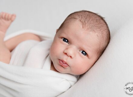 Cute baby wrapped up like a turtle whilst pouting and looking at the camera.