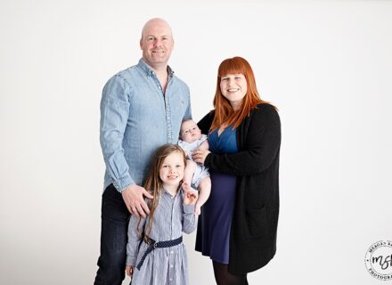 mum dad big sister and baby on white background all facing the camera smiling