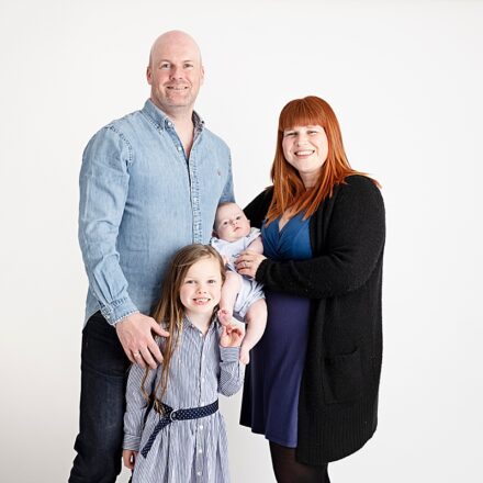 mum dad big sister and baby on white background all facing the camera smiling