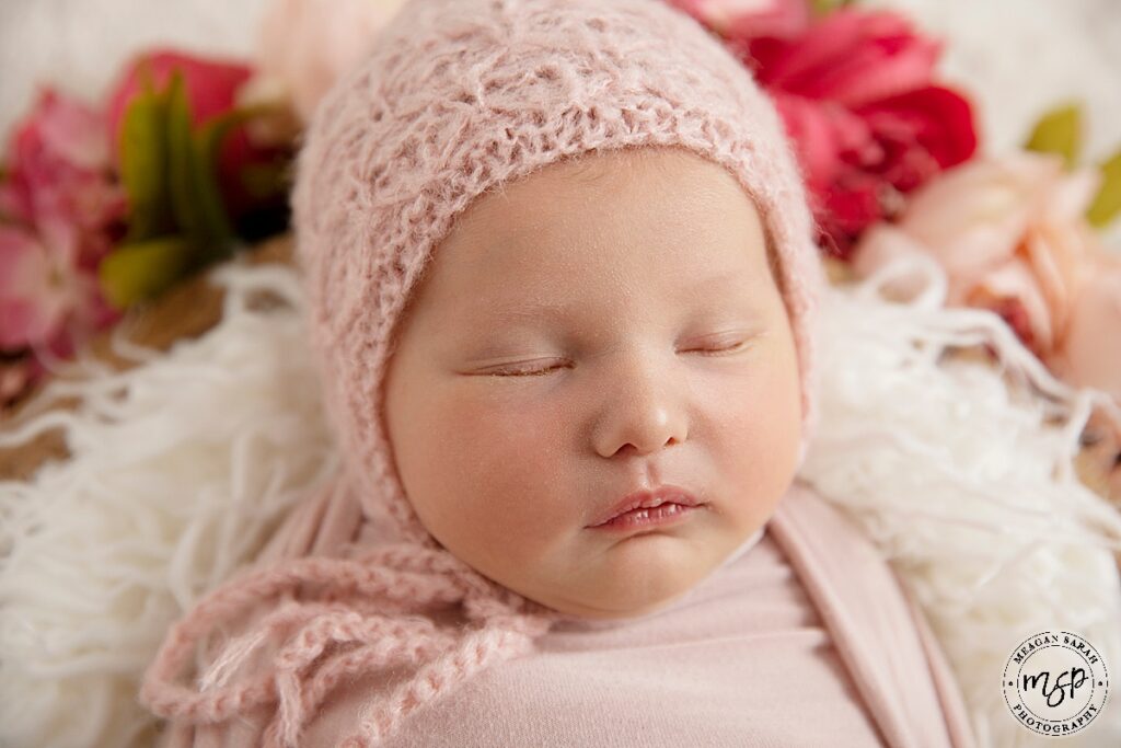 Sleeping baby in a bowl with flowers and pink bonnet.