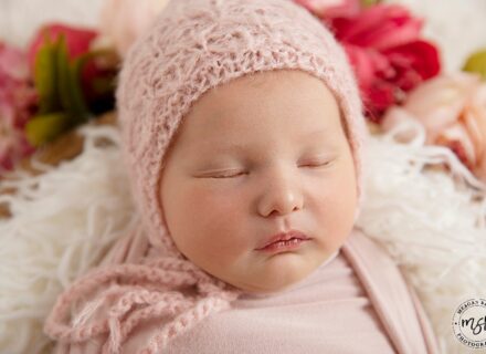 Sleeping baby in a bowl with flowers and pink bonnet.