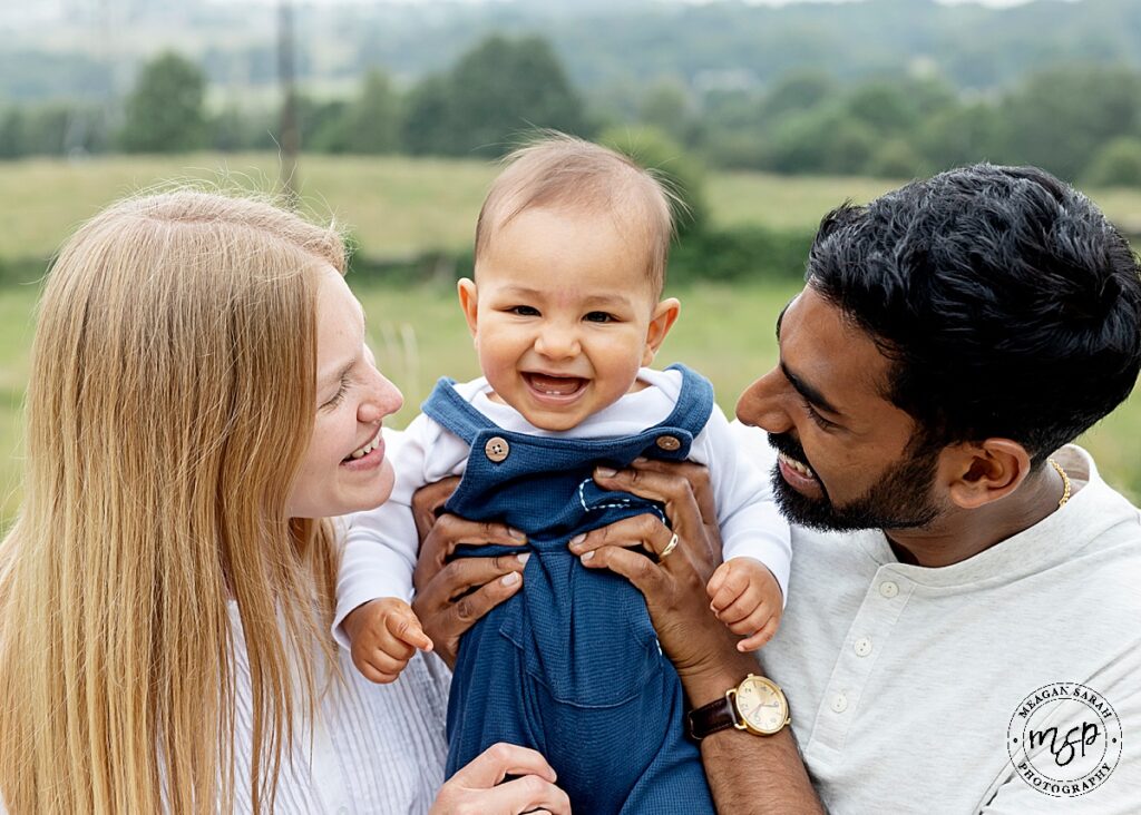 image of handsome baby boy at his family mini shoot on location. Grass in background. Parents holding child. Happy family. Leeds.