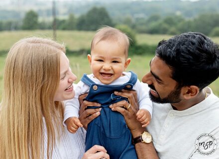 image of handsome baby boy at his family mini shoot on location. Grass in background. Parents holding child. Happy family. Leeds.