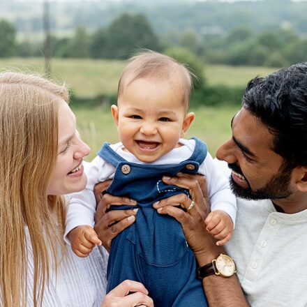 image of handsome baby boy at his family mini shoot on location. Grass in background. Parents holding child. Happy family. Leeds.