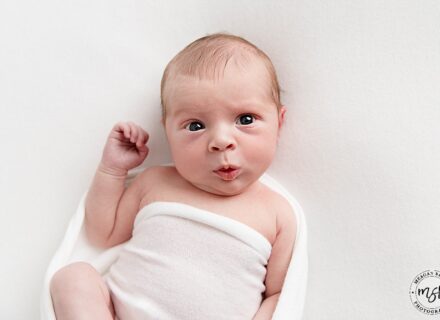 baby boy of white background with white fabric over him pouting to the camera