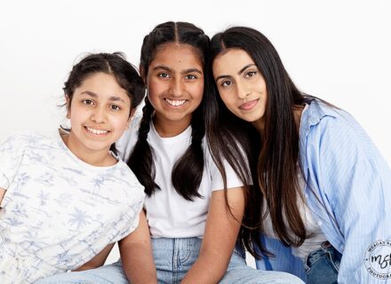 three sisters facing the camera smiling, heads touching, in blue and white outfits all with dark black hair