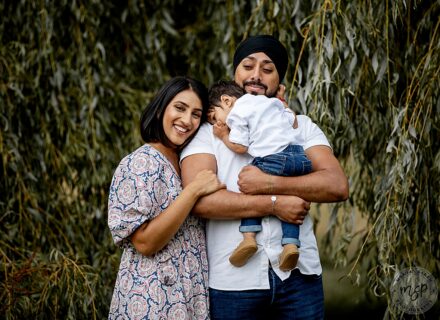 mum dad and toddler under a willow tree dad holding son mum cuddling them smiling at camera