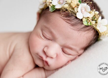 close up of baby girls face sleeping with hand under head wearing a delicate floral headband