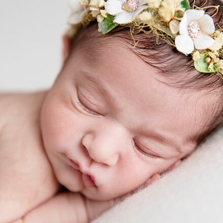 close up of baby girls face sleeping with hand under head wearing a delicate floral headband