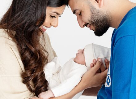 mum and dad holding newborn together in between them looking down at baby