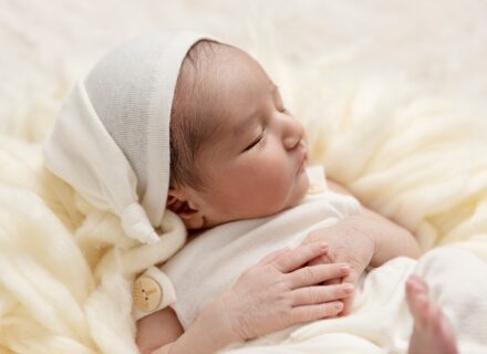 newborn baby asleep in cute sleepy outfit cream