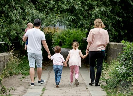 family of five walking away, we can see their backs all holding hands against a greenery setting