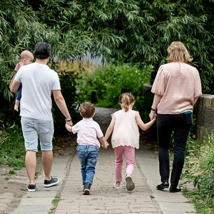 family of five walking away, we can see their backs all holding hands against a greenery setting