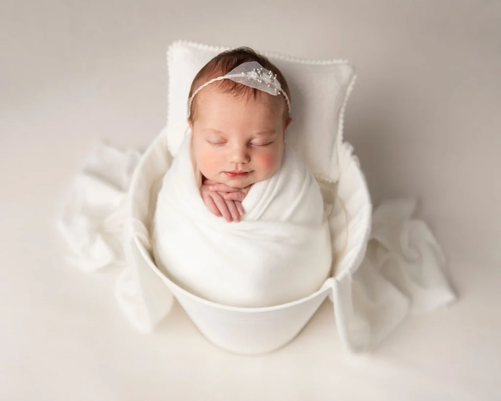 newborn baby asleep, swaddled in white and cream.