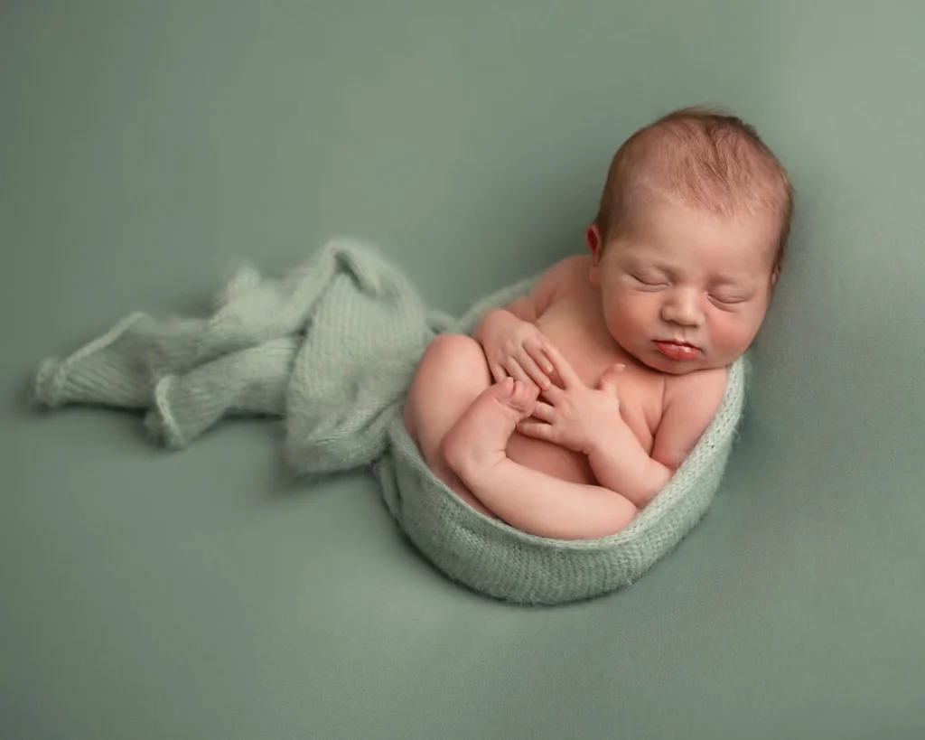 baby sleeping on his back on sage green background.