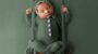Baby photographer Leeds. Beautiful newborn photography Leeds. Photo of a newborn baby sitting on a wooden and macrame swing. Wearing a knitted button down onsie and knitted bonnet. All one colour of sage green.