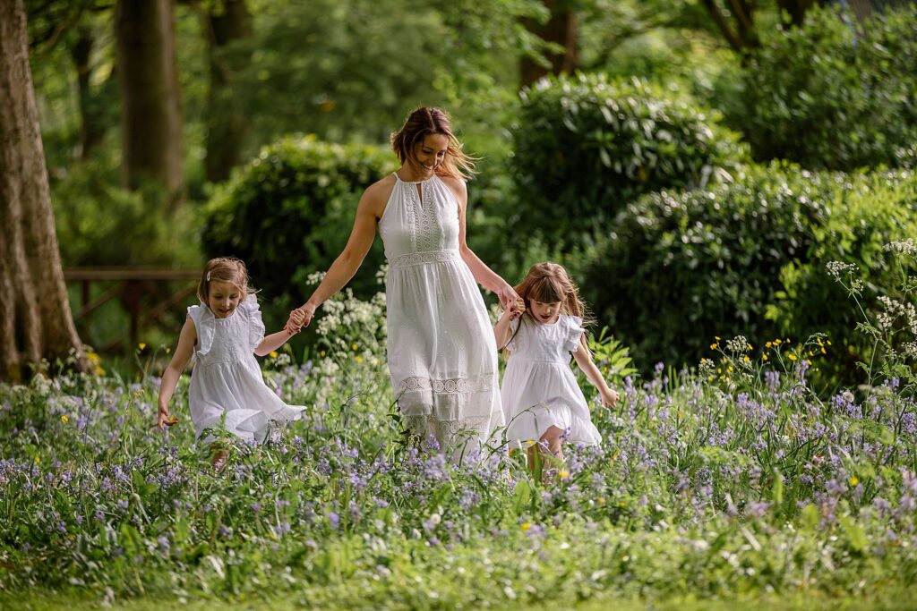 Beautiful image of a mother and her two daughters all in white running through long grass. Photograph taken and Kirkstall Abbey Leeds. Part of our Mummy and Me photoshoot sessions. mini session. outdoor photography.