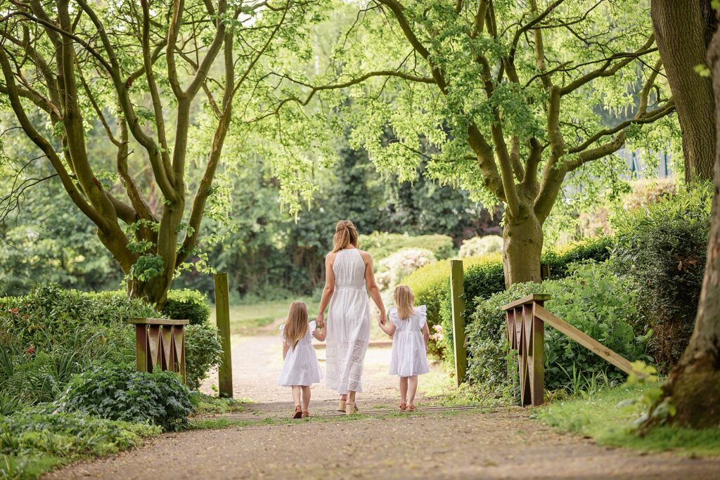 beautiful photo of mother with two daughters walking away down a path over a bridge. all wearing white. photoshoot outdoors. taken at Kirkstall Abbey, Leeds. 