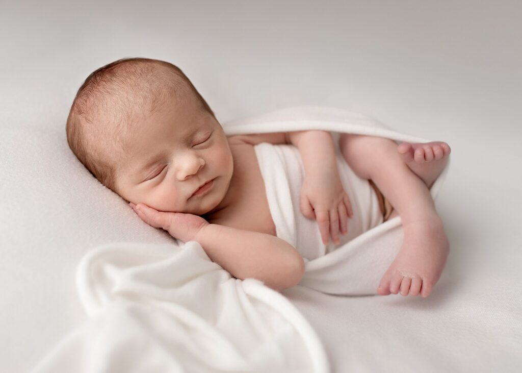 professional photography in Leeds of newborn baby asleep on white with a white swaddle.