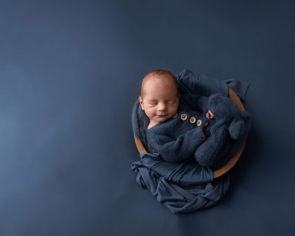 sleeping newborn in a wooden basket. asleep on a blue background with a blue outfit.