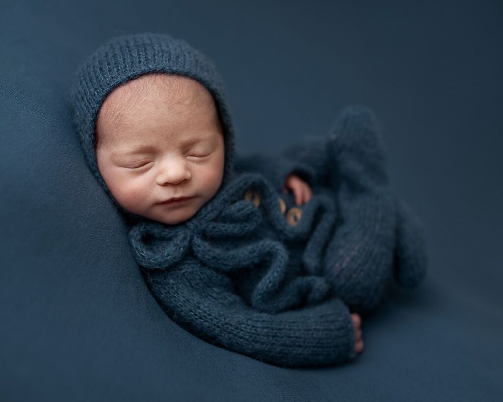 sleeping baby newborn boy professional photoshoot. Laying on blue. On his back.