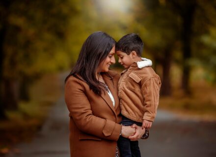 autumn family photo. A mother and child touching foreheads. Wearing warm tones for an autumn photoshoot in Leeds, Roundhay Park. standing on a long tree lined path.