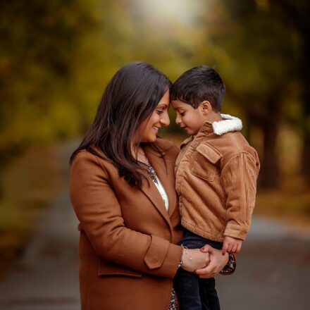 autumn family photo. A mother and child touching foreheads. Wearing warm tones for an autumn photoshoot in Leeds, Roundhay Park. standing on a long tree lined path.