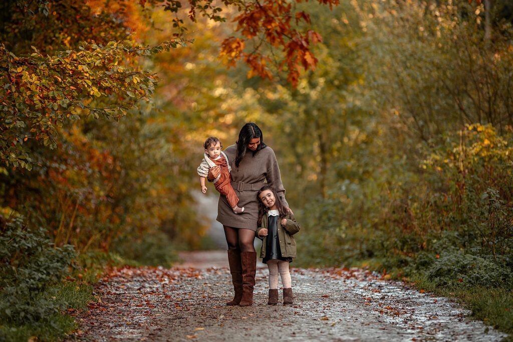 Autumn family photoshoot in Otley Chevin near Leeds – a mother holding her two children playing under colourful autumn fall leaves. 