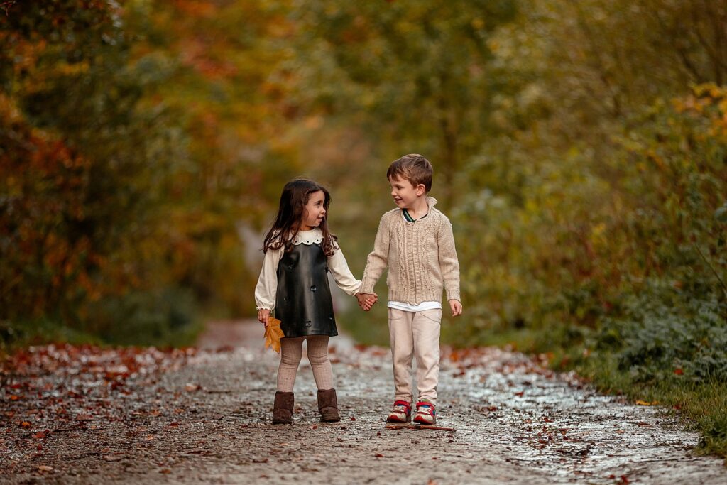 Autumn family photoshoot in Otley Chevin near Leeds – two children holding hands as they prepare to run down the bridal path towards the camera under colourful autumn fall leaves. 