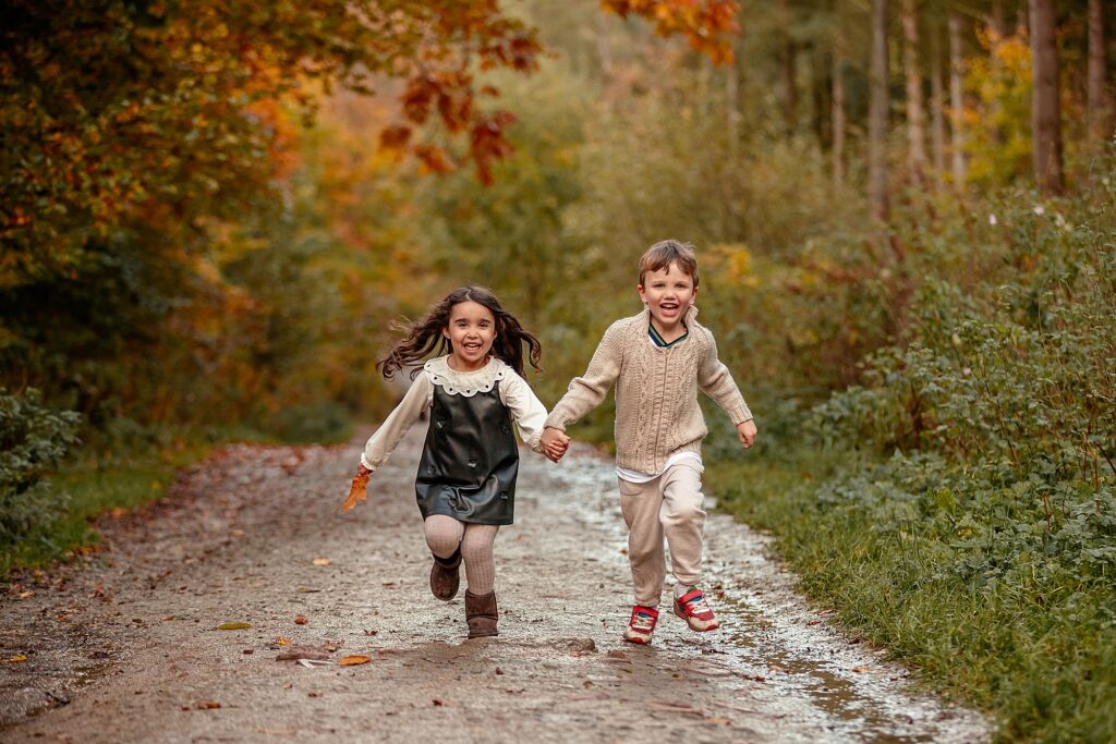 Autumn family photoshoot in Otley Chevin near Leeds – two children playing, holding hands and running towards the camera under colourful autumn fall leaves. On a bridal path.